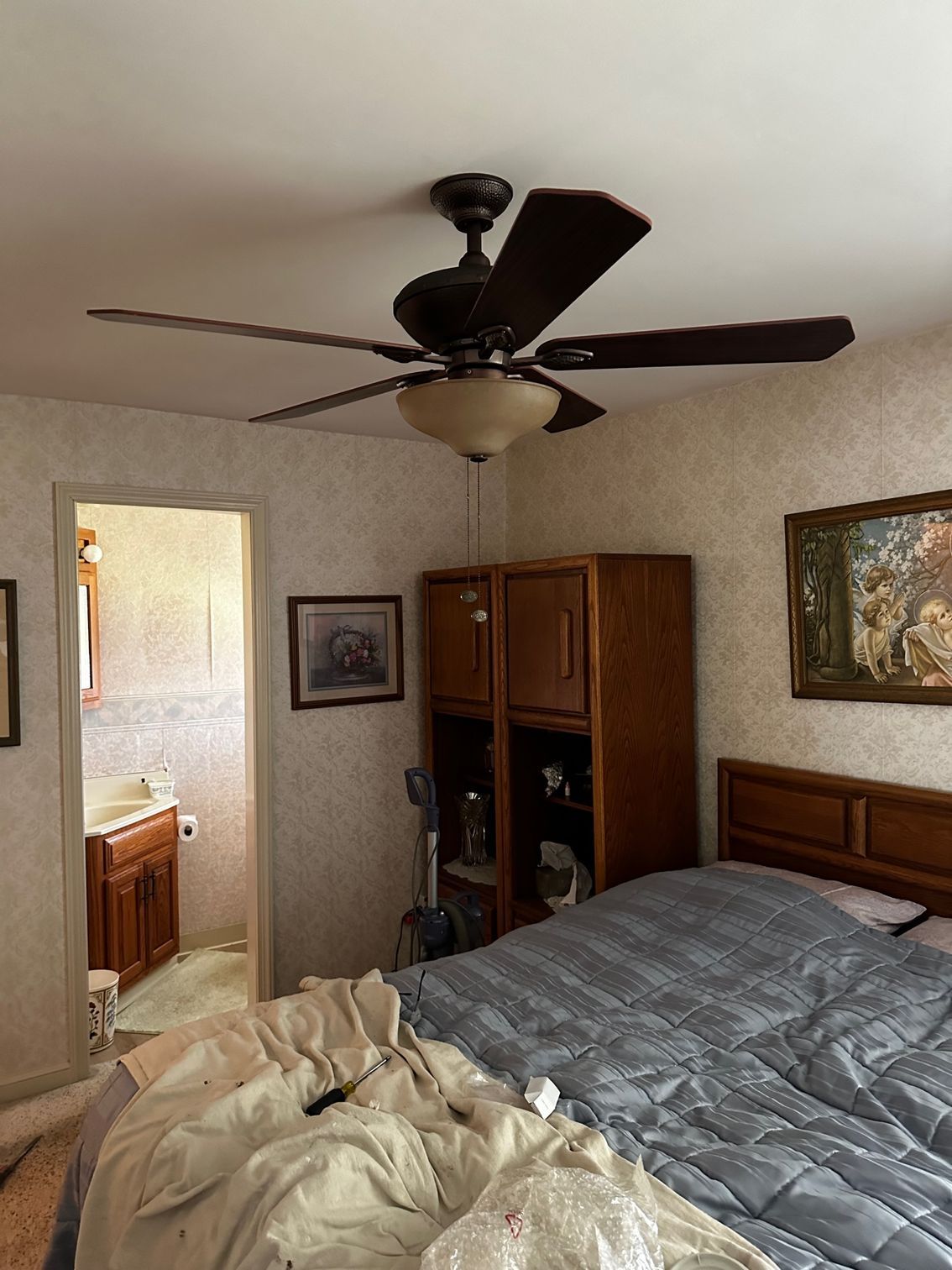 Bedroom with unmade bed, ceiling fan, wooden dresser, and open bathroom doorway