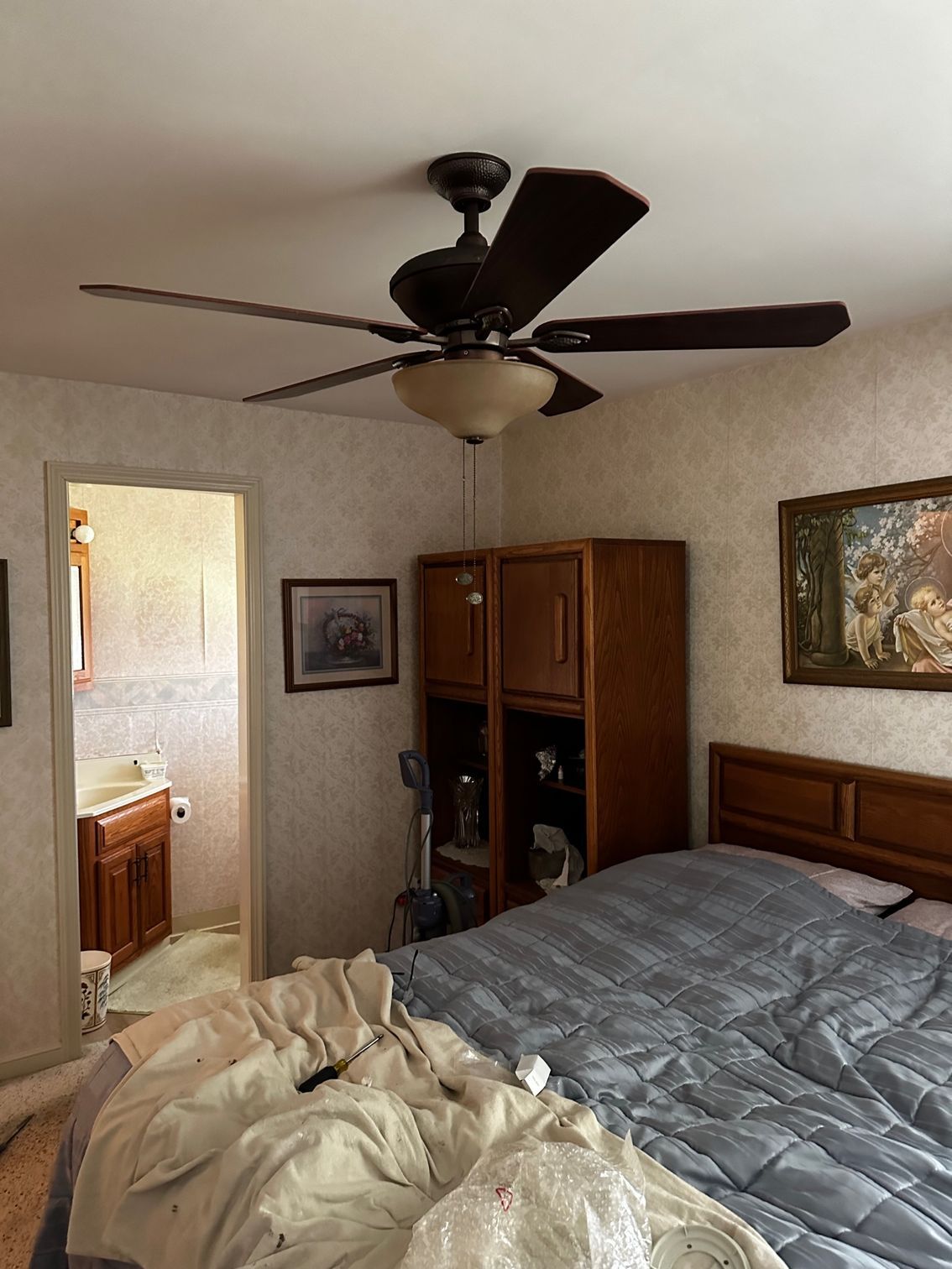Bedroom with unmade bed, ceiling fan, wooden dresser, and open bathroom doorway