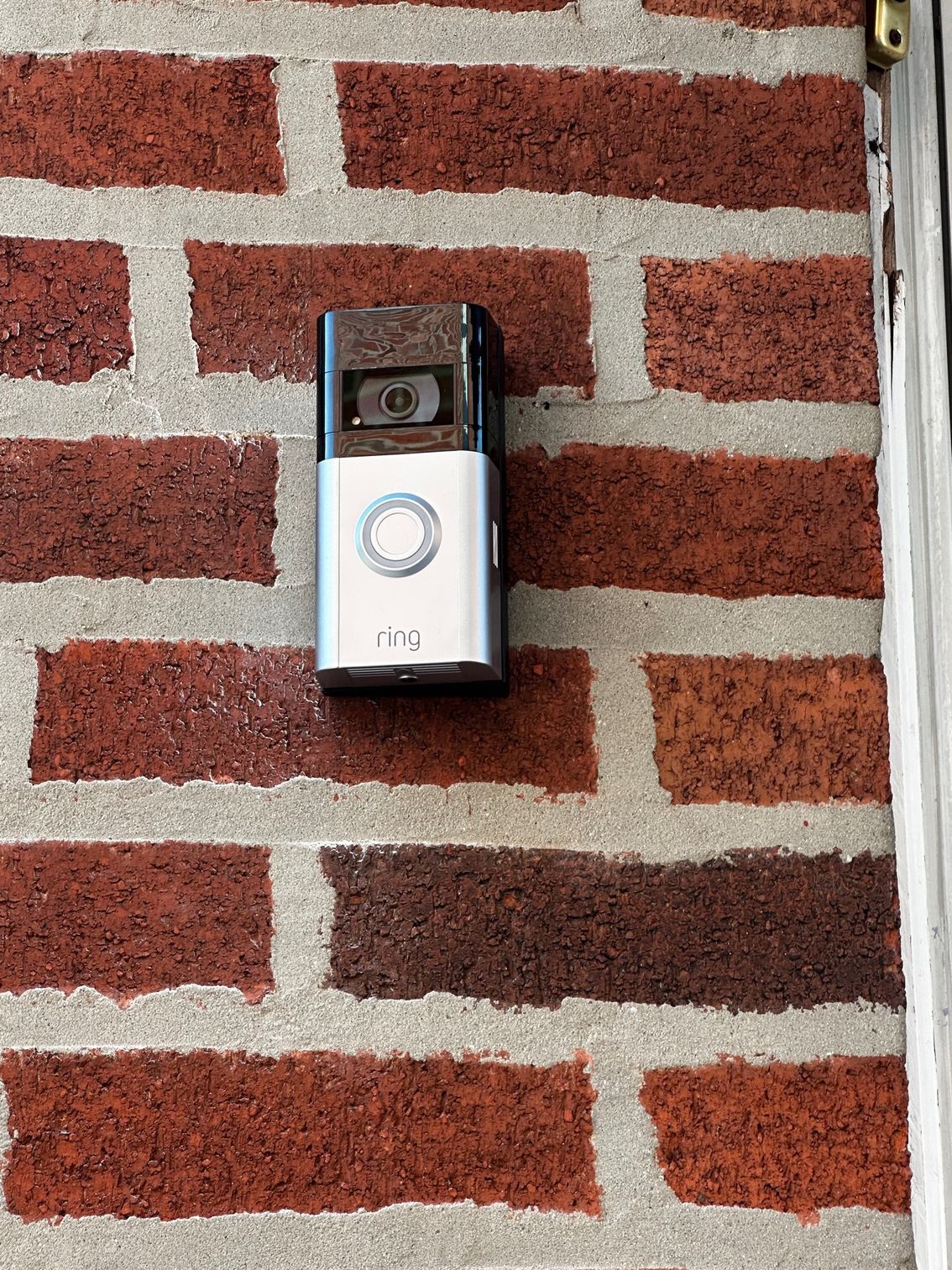 Video doorbell mounted on a red brick wall with a circular button and camera lens.