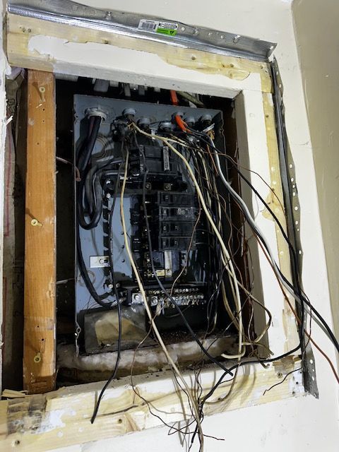 Open electrical panel with exposed wiring in a wall opening