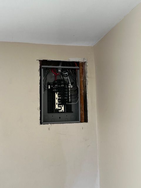 Open electrical panel in a beige wall with exposed wiring and removed cover plate