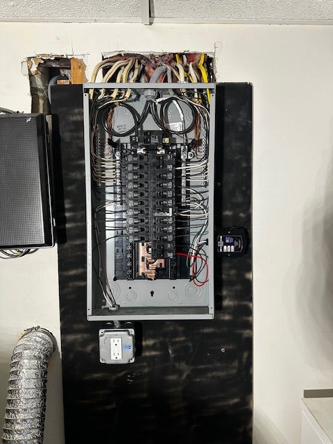 Open electrical panel with wiring and breakers mounted on a black wall