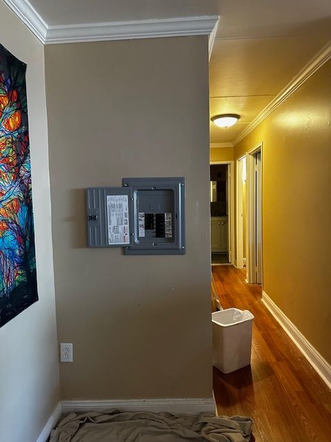 Hallway with beige walls, wood floor, electrical panel, and colorful wall art on the left.