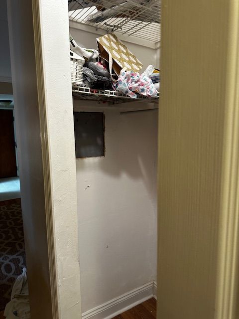 Open closet with shelves holding clutter and a dark square opening on the back wall