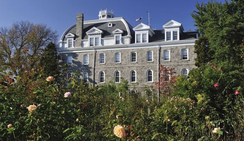 Stone building with dormer windows behind a garden of pink roses under a blue sky