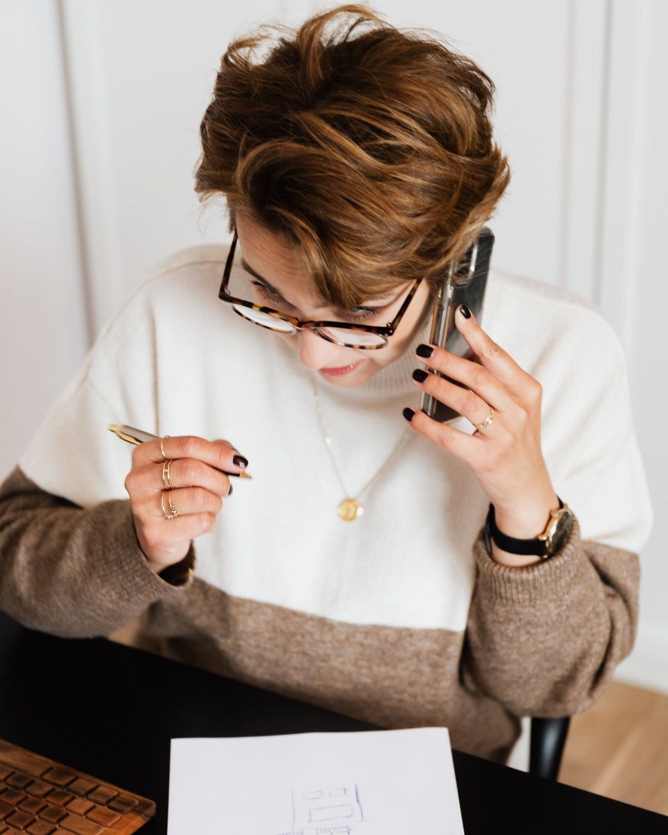Person in glasses looking at papers and talking on a phone at a desk.