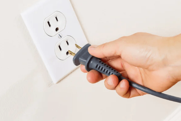 Hand plugging a black electrical cord into a white wall outlet