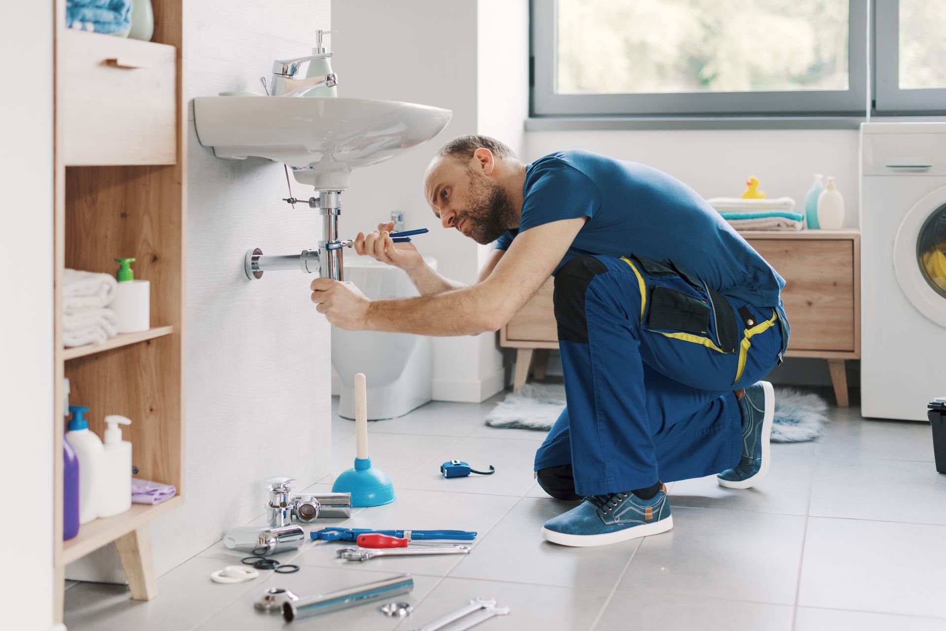 Close-up of plumber, from a plumbing company, repairing the sink with a tool in a bathroom. Plumber repairing a sink under a white bathroom vanity, with tools scattered on the floor.