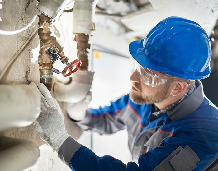 A man wearing a hard hat and safety glasses is working on a pipe. — Elgin, IL — All Suburban Emergency Plumbing A man wearing a hard hat and safety glasses is working on a pipe. — Elgin, IL — All Suburban Emergency Plumbing