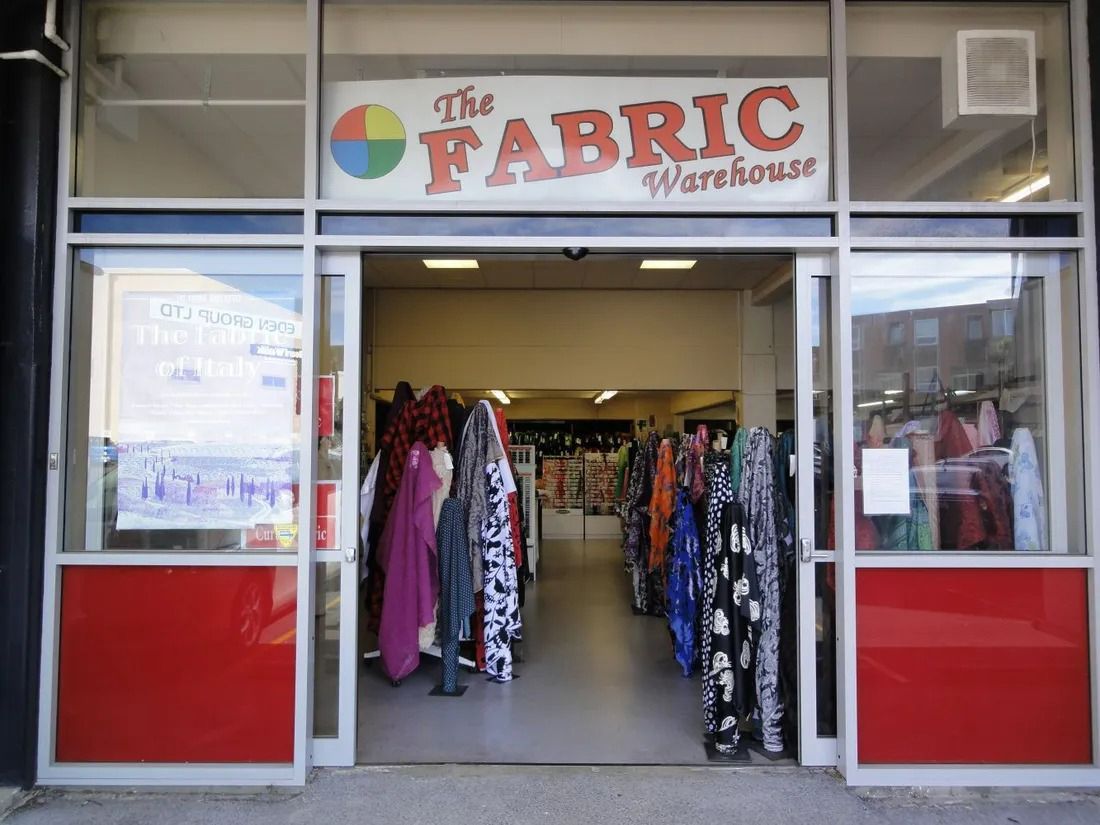 Entrance to The Fabric Warehouse store with fabric rolls visible. Red and glass exterior.