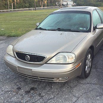Gold Mercury Sable sedan parked on asphalt next to a grassy area.