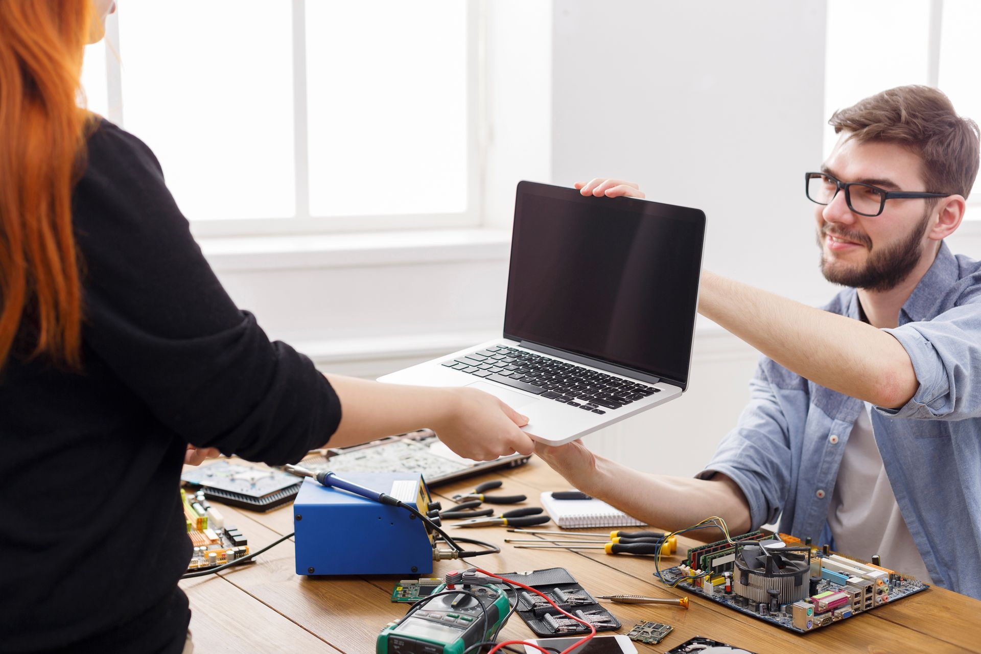 A technician giving a repaired laptop to an out-of-view client.