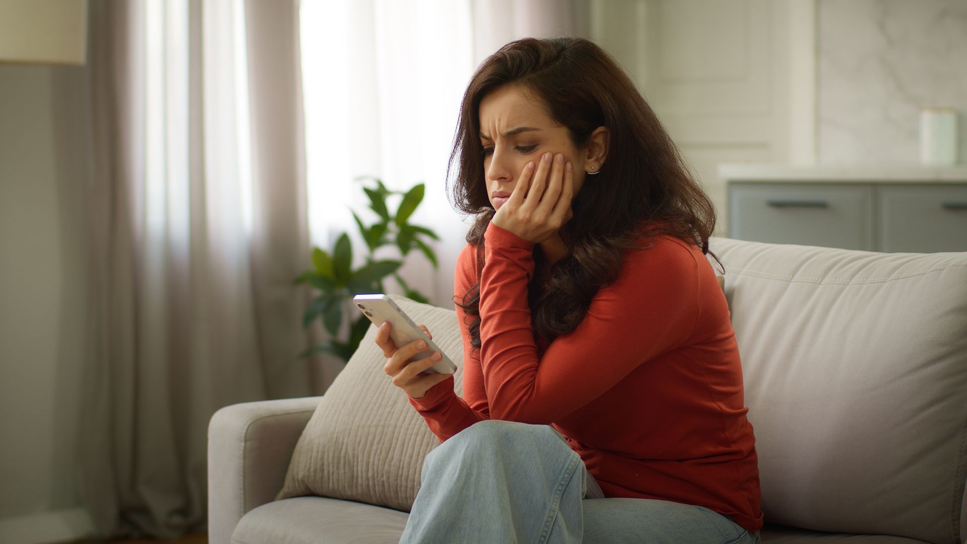 An upset woman holding a mobile phone reacting to a no connection failure, seated on her couch.