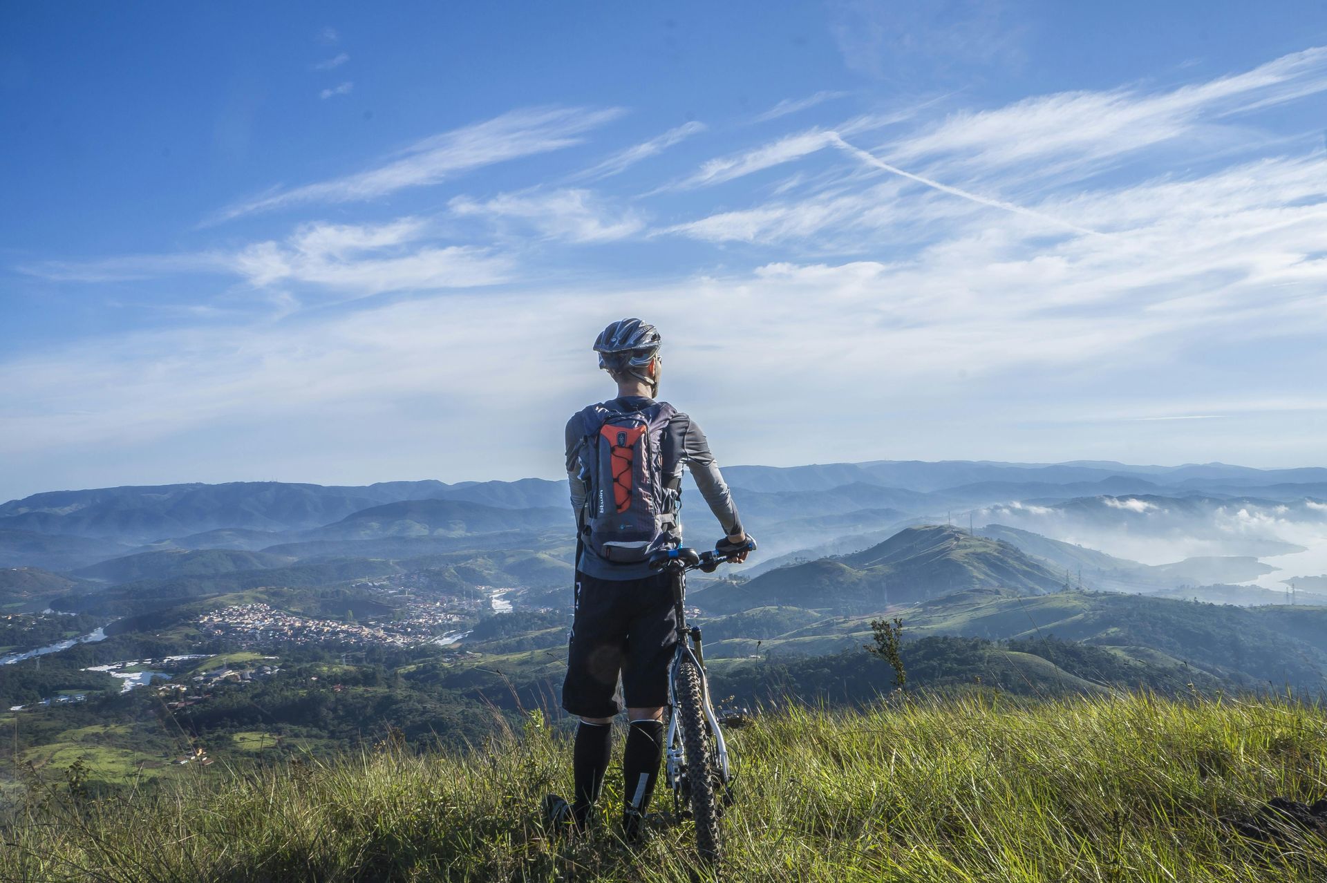 Mountain biker overlooking a scenic landscape of green hills and a town, under a blue sky.