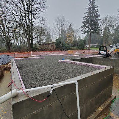 Construction site foundation with gravel fill, concrete walls, pink insulation, and piping.