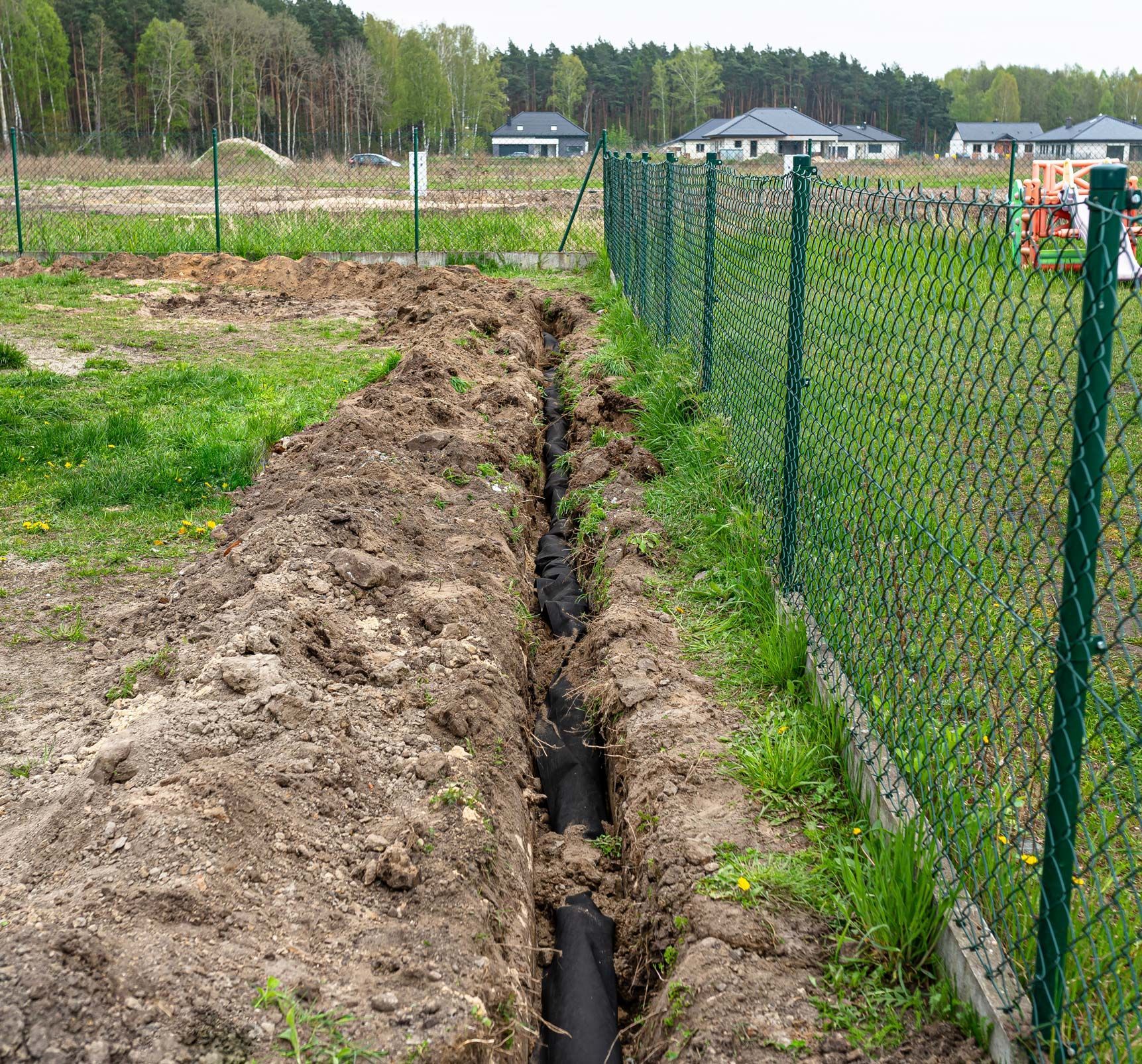 A trench dug in the yard along the fence to lay the drainage pipe. A trench dug in the yard along the fence to lay the drainage pipe.