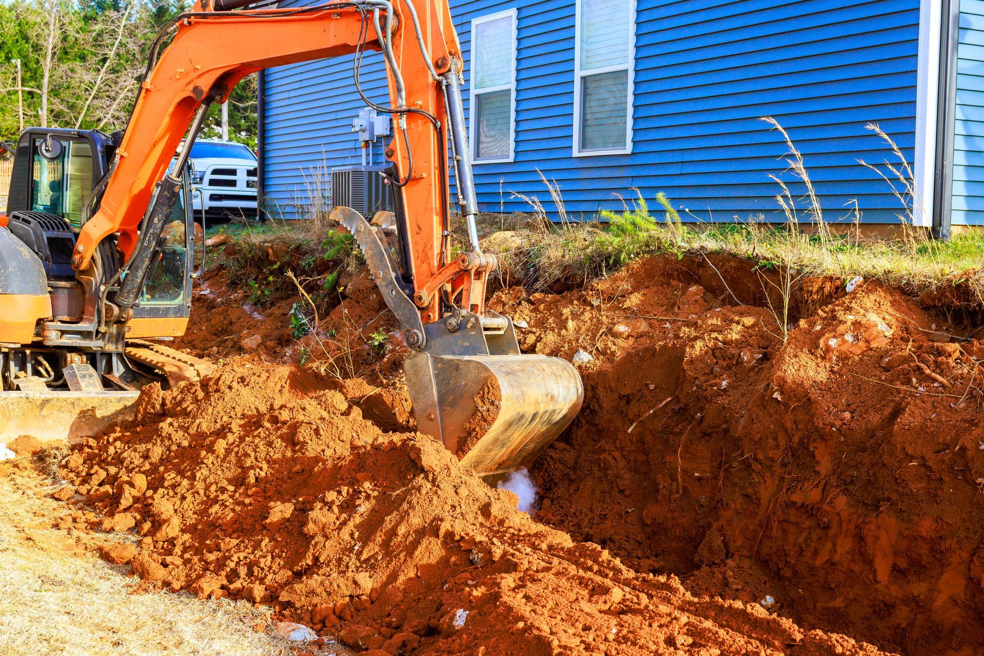 An excavator digs a trench near a building in a residential construction area. An excavator digs a trench near a building in a residential construction area.