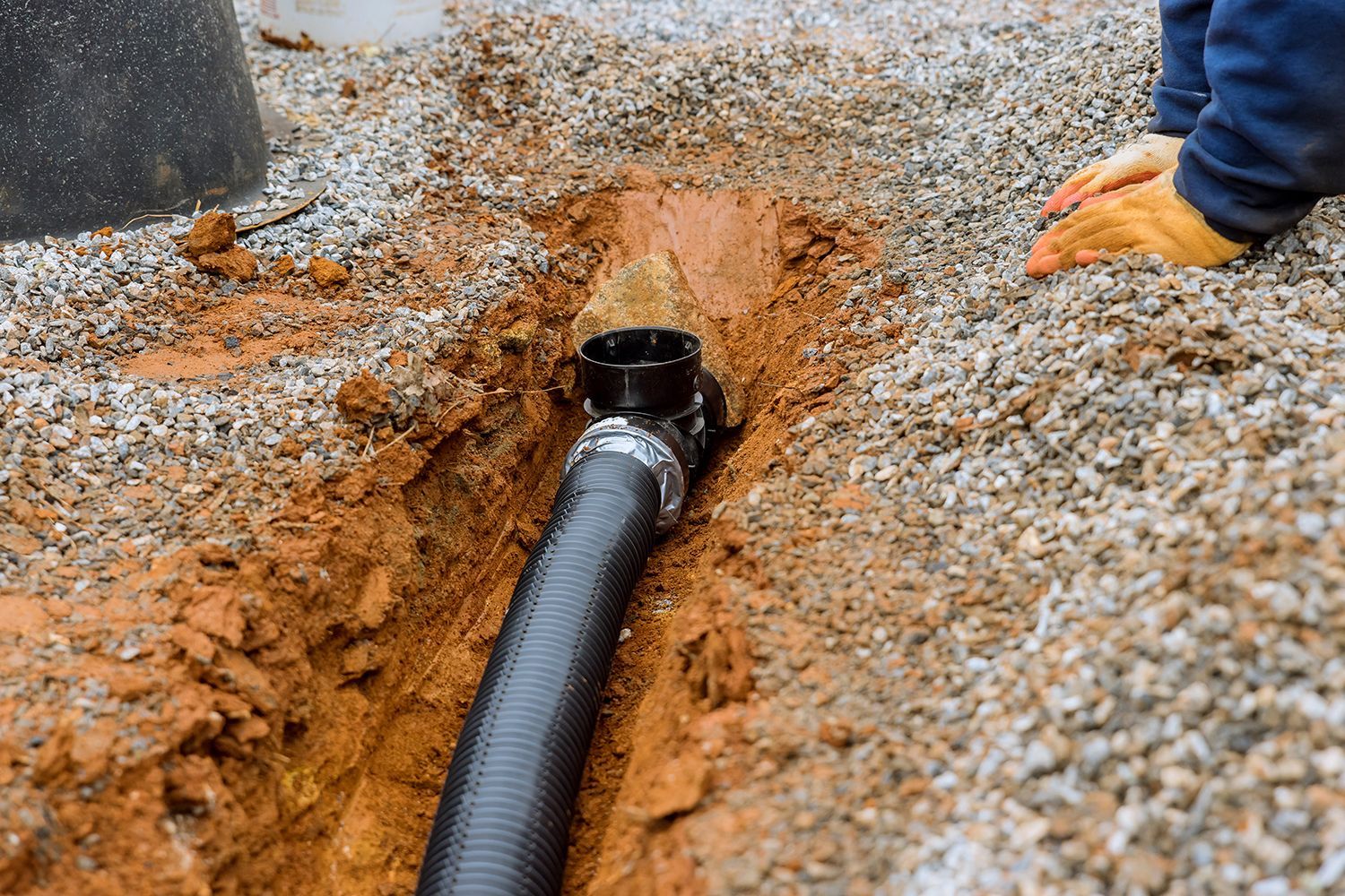 Worker connecting corrugated drain pipe to catch basin in gravel trench. Worker connecting corrugated drain pipe to catch basin in gravel trench.