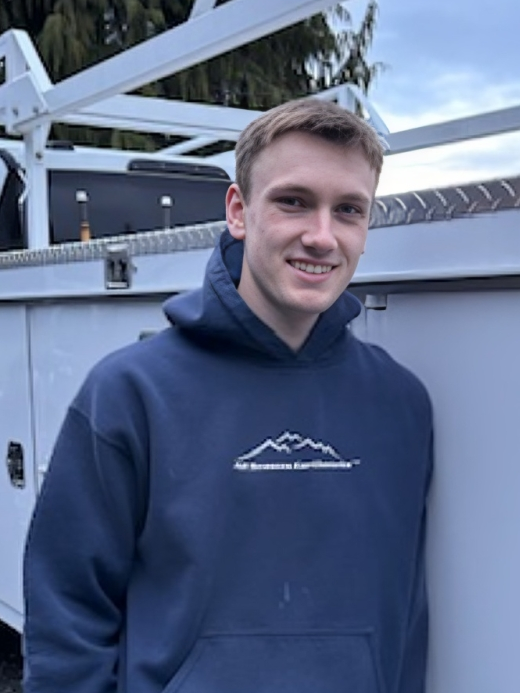 Young man in navy hoodie smiles, leaning against a utility truck.