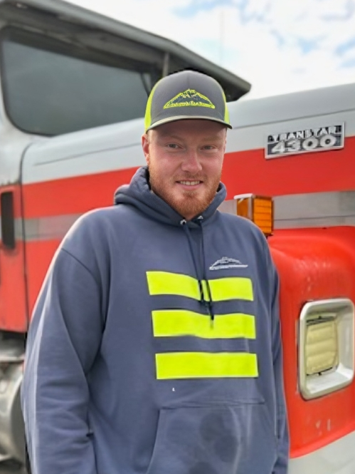 Man in blue hoodie and cap, standing by a red and white semi-truck.