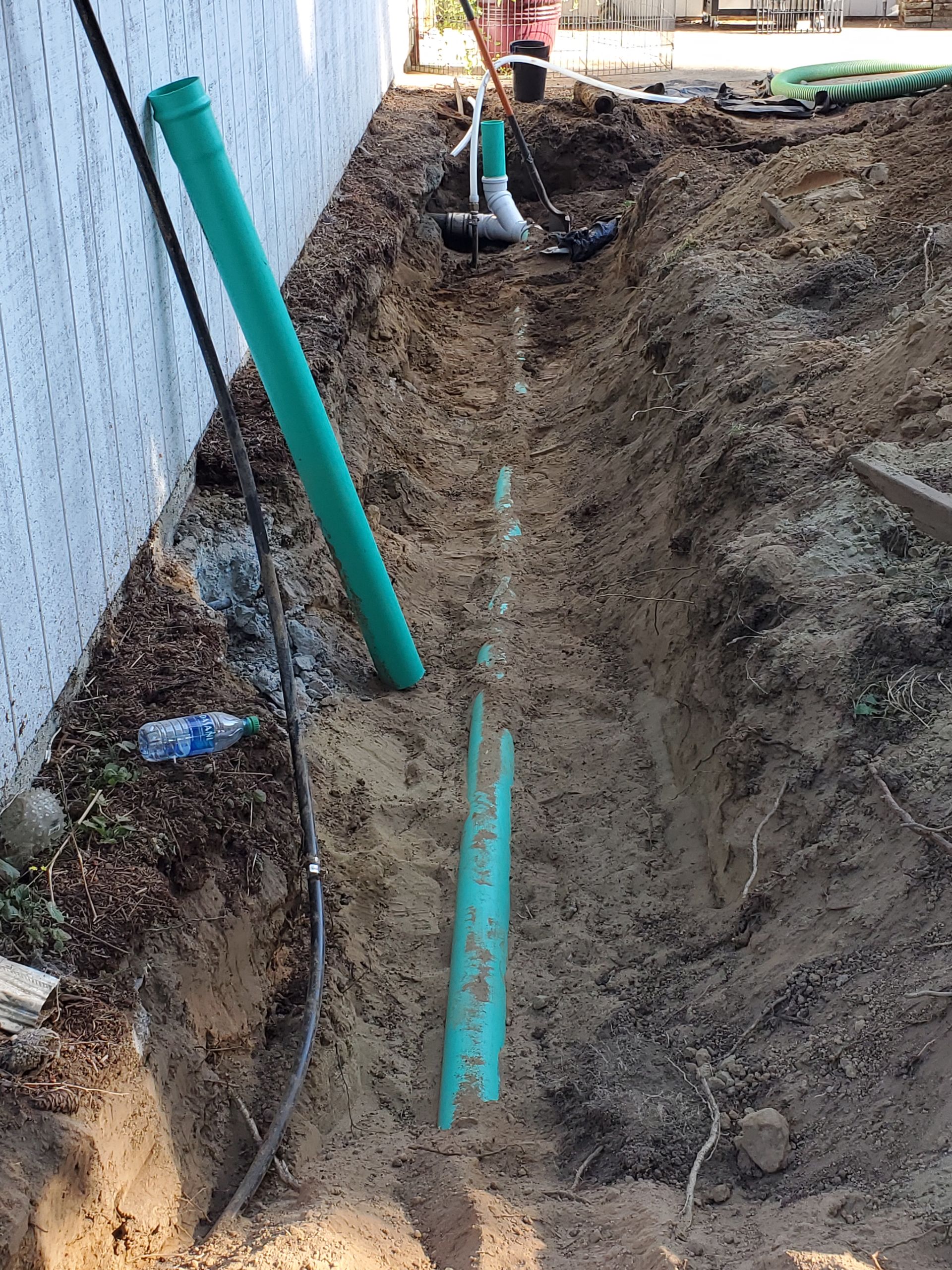 Trench with green pipes and black cable next to white wall. Construction site.