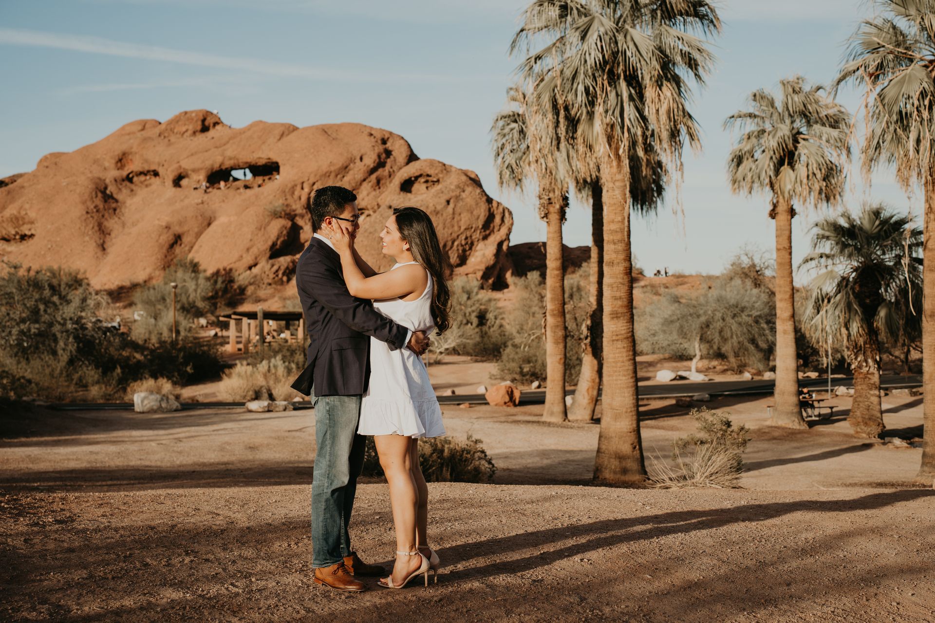 A man and woman are kissing in front of a mountain and palm trees.
