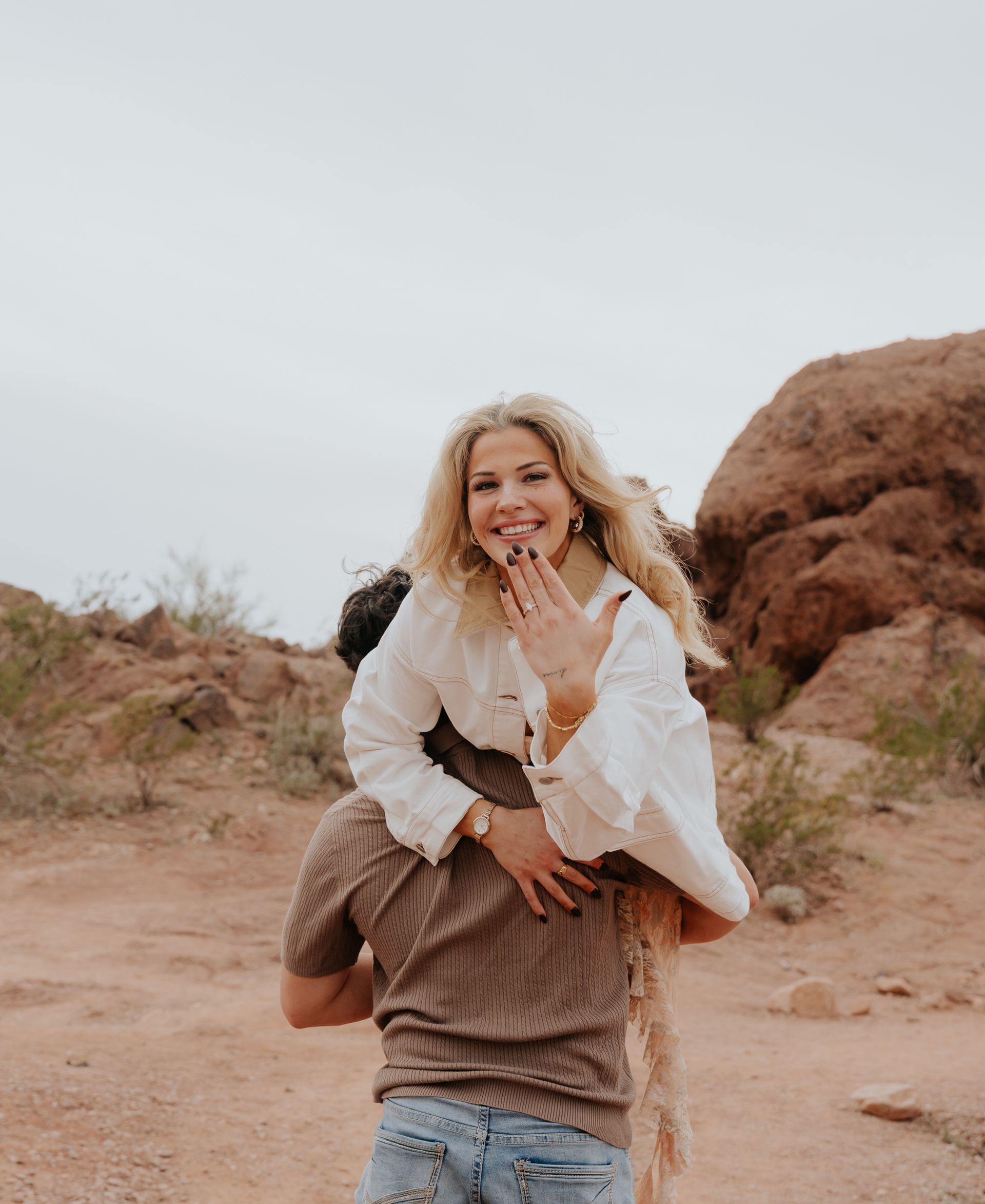 A man and woman are kissing in front of a mountain and palm trees.