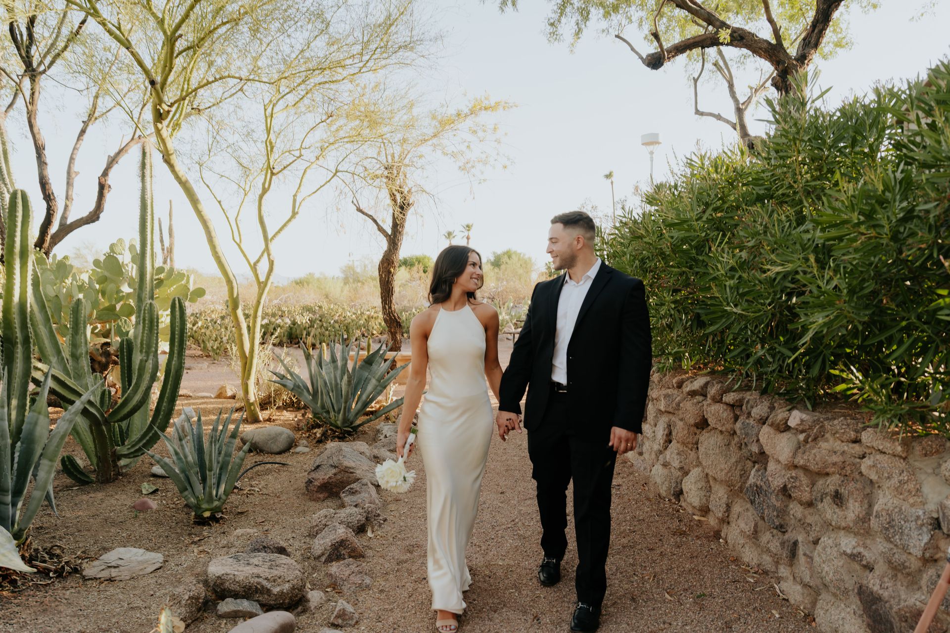 A bride and groom are walking in the desert holding hands.