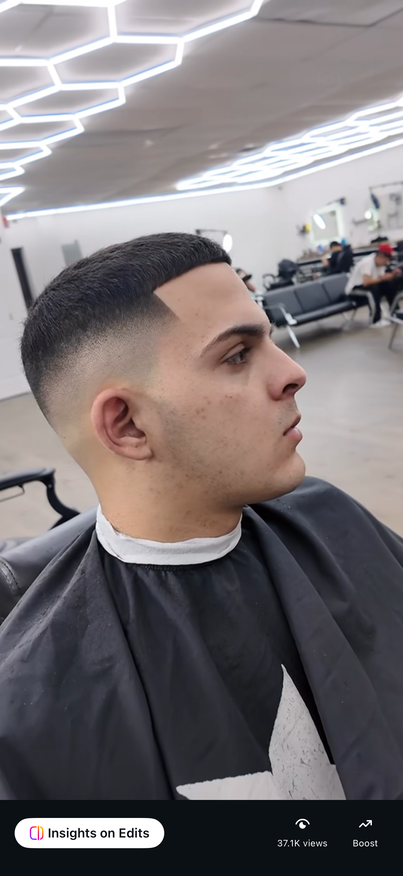 Side-profile portrait of a man in a barbershop, wearing a black cape with a fresh fade haircut.