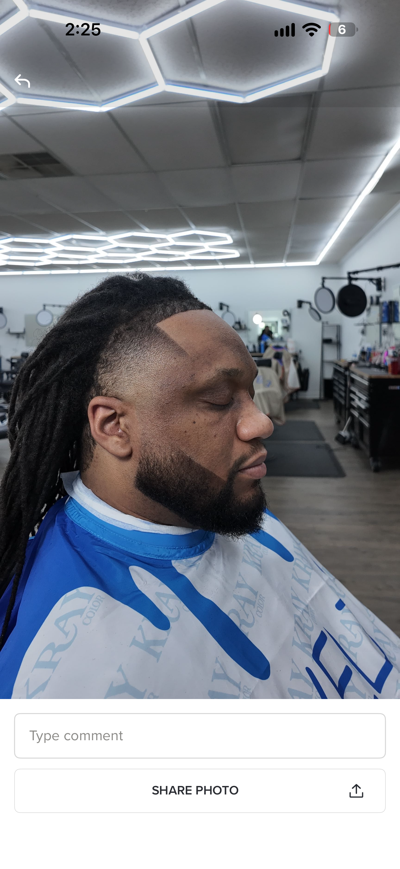Man in blue jersey getting a haircut in a barbershop, shown in profile under bright ceiling lights