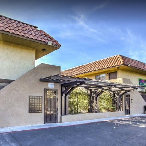 Apartment building entrance with black pergola walkway, tan stucco walls, and red tile roofs