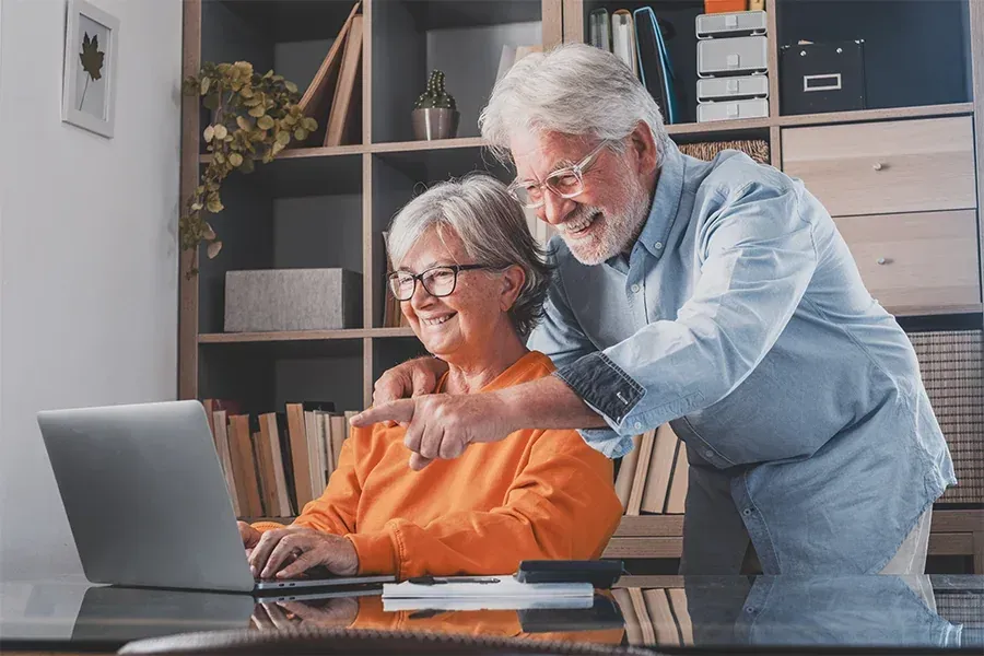Two older adults smiling at a laptop in a home office