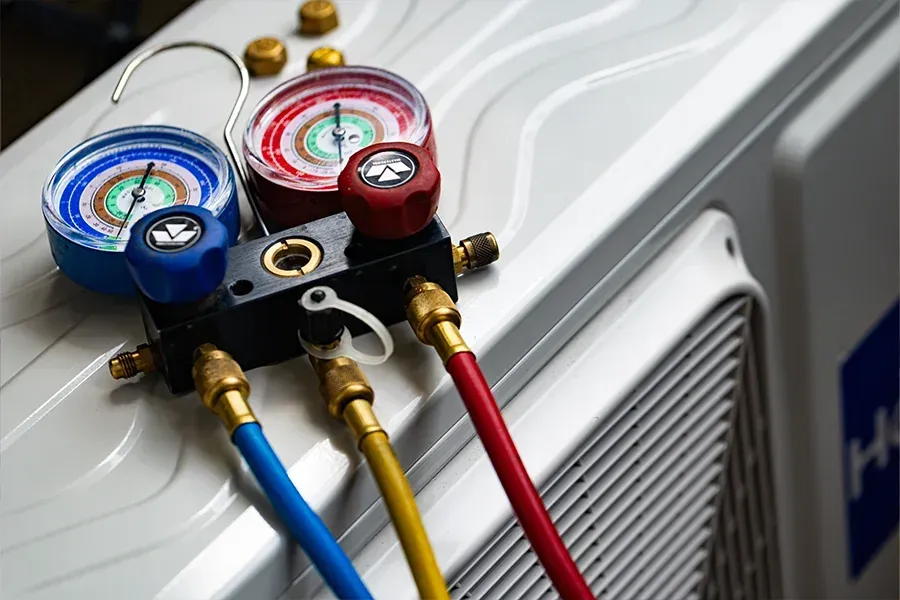 HVAC refrigerant manifold gauges with blue, yellow, and red hoses attached to a unit
