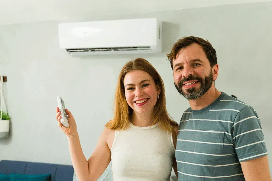 Smiling couple holding a remote in front of a wall-mounted air conditioner