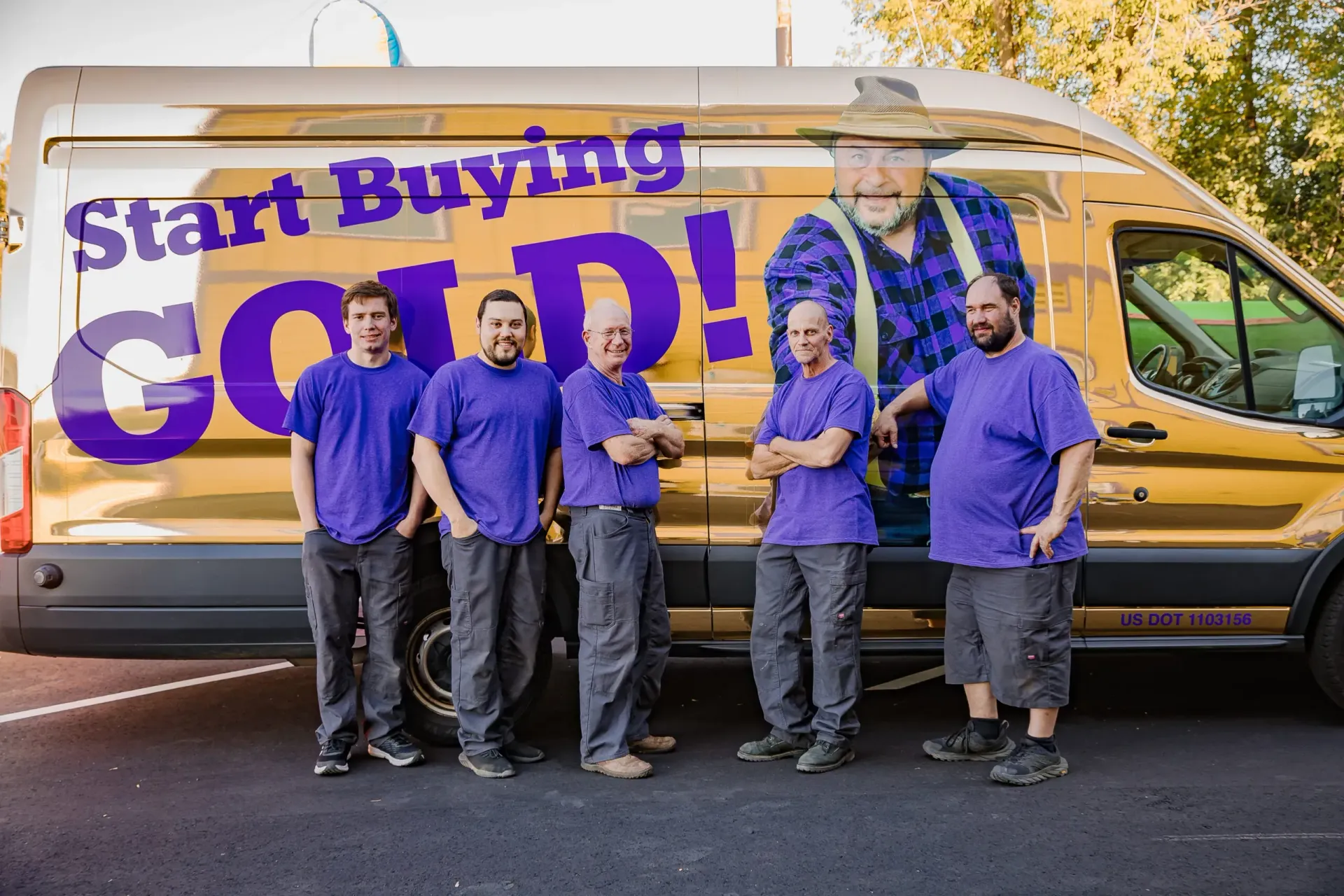 Five people in purple shirts stand in front of a van with “Start Buying GOLD!” written on the side.
