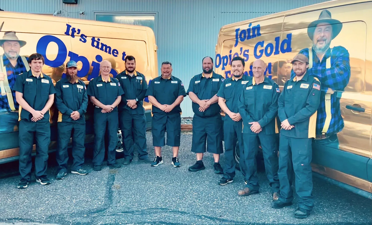 Group of workers standing in front of a blue-and-yellow “Join Opi’s Gold” truck, smiling at the camera.