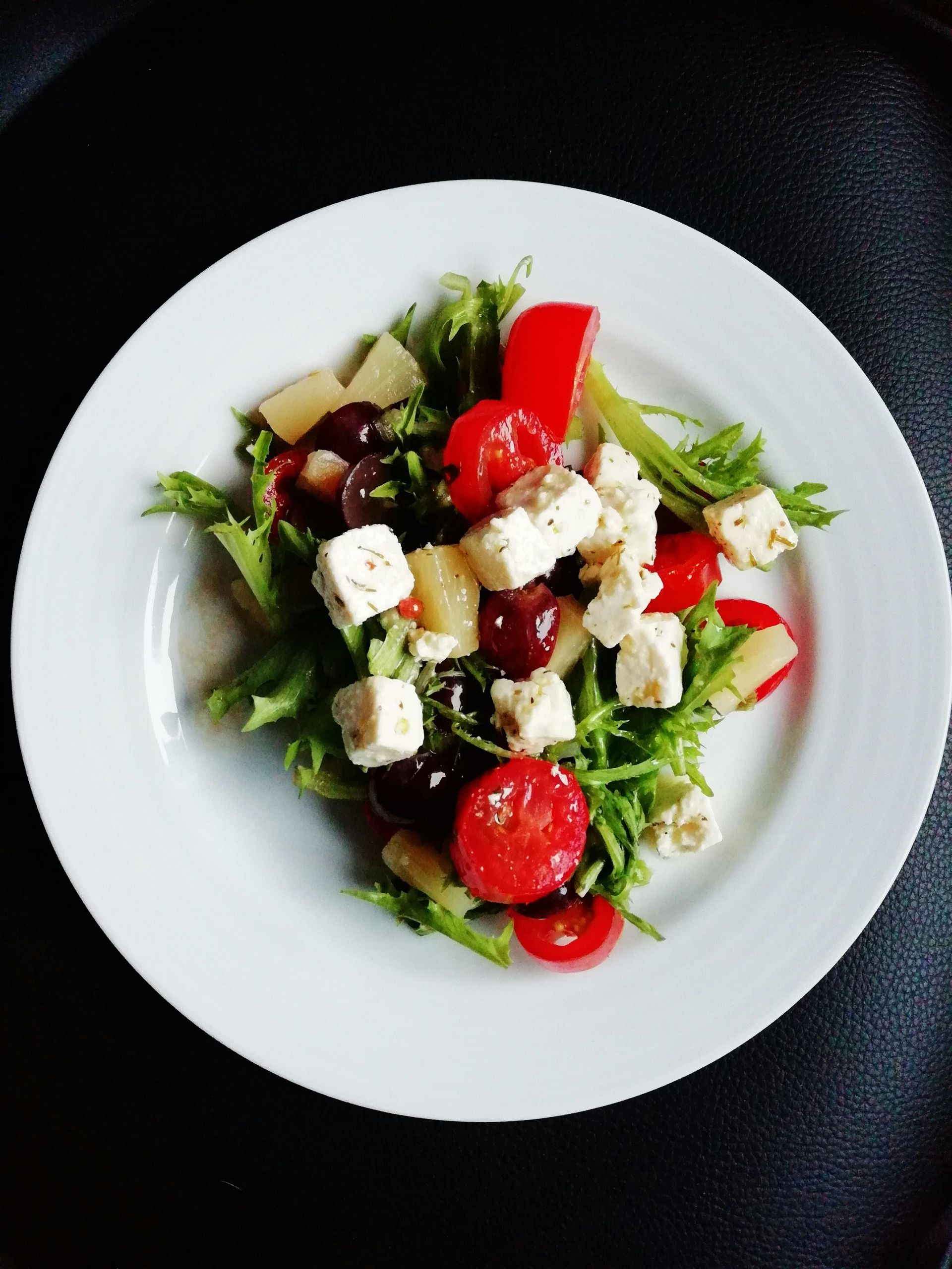 Greek salad with tomatoes, cucumber, feta, and greens on a white plate
