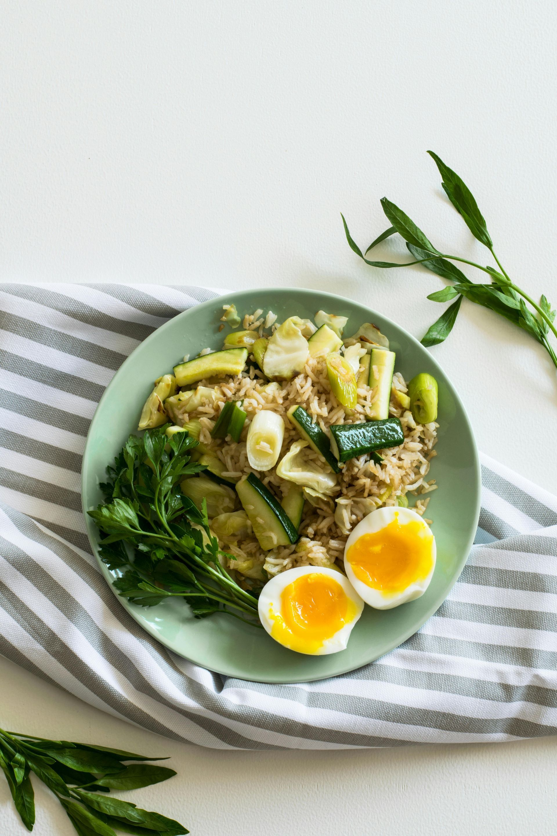 Green salad bowl with soft-boiled eggs on a striped cloth, with herb sprigs on a white table