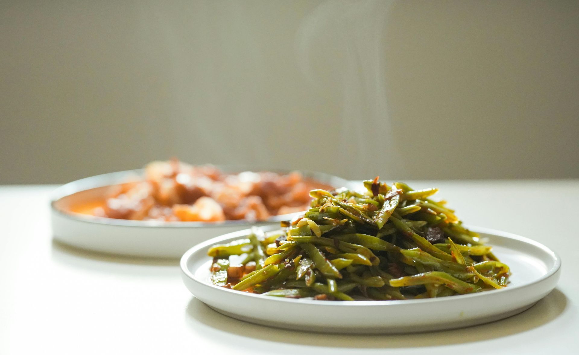 Plates of cooked vegetables and shrimp on a bright tabletop, with green beans in focus