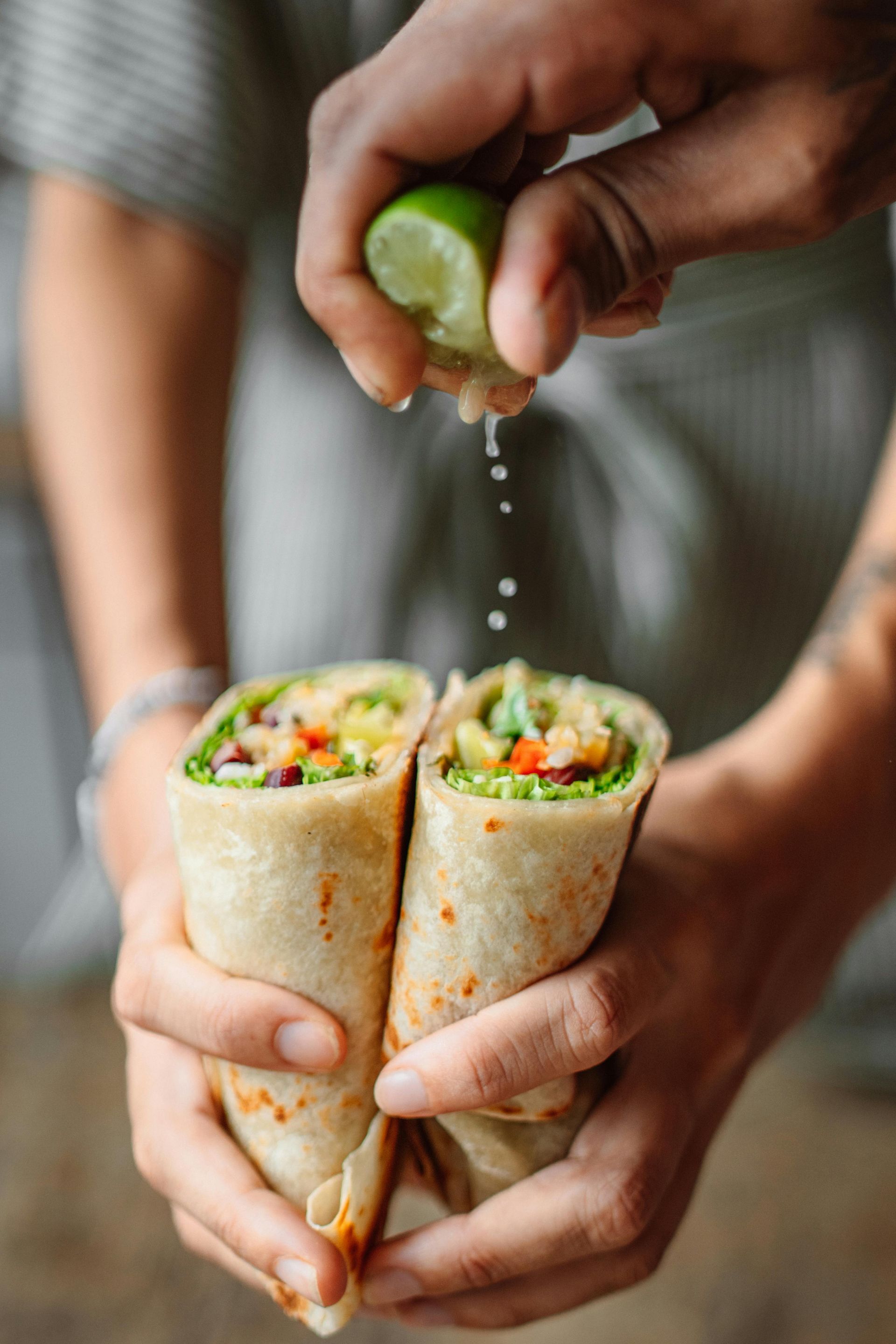 Hands squeezing lime over two vegetable wraps held together
