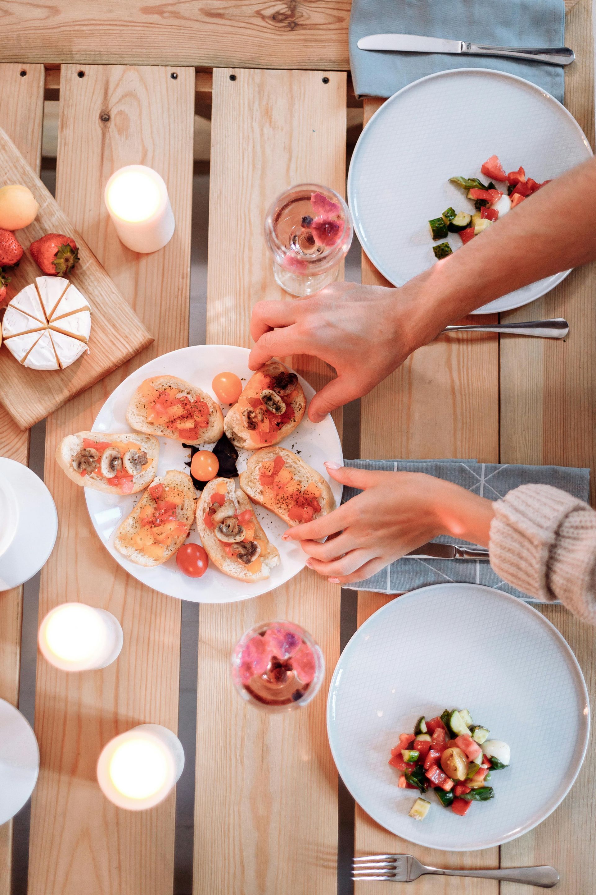 Hands sharing pastries and drinks around a wooden table with plates of dessert and salad.