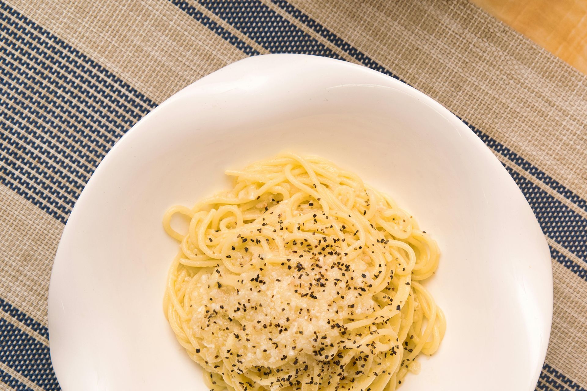 Plate of creamy spaghetti with black pepper on a striped placemat