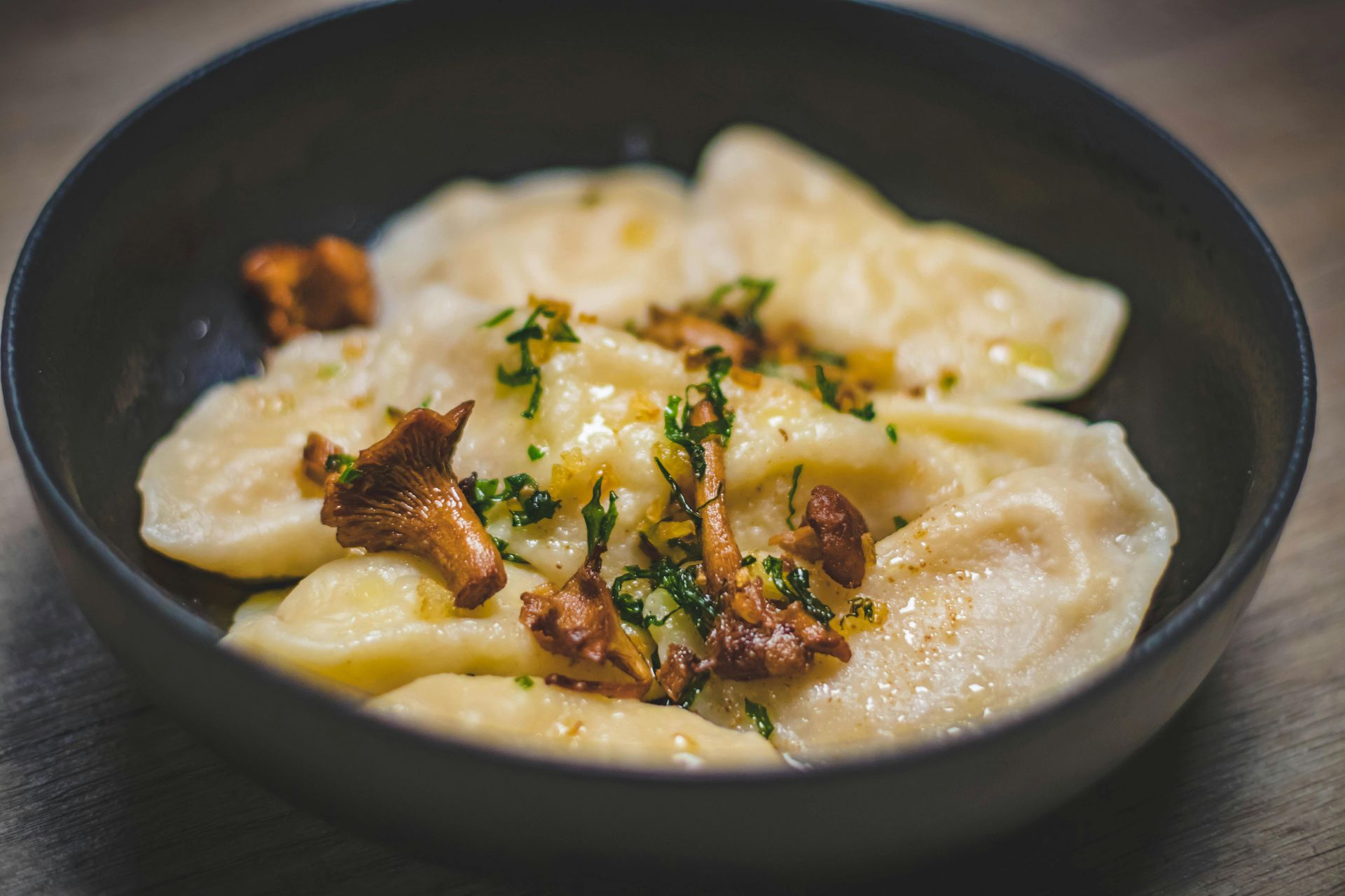 Creamy dumplings in a black bowl topped with herbs and crispy mushrooms