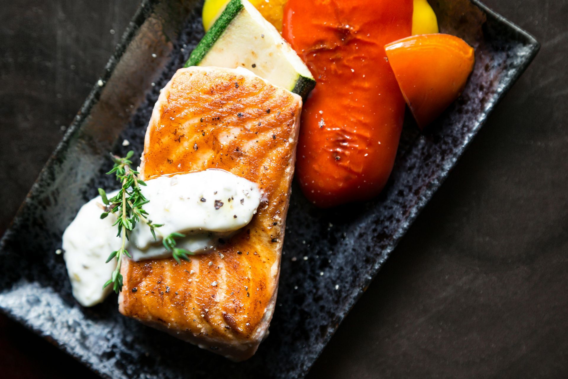 Seared salmon with white sauce and vegetables on a black plate