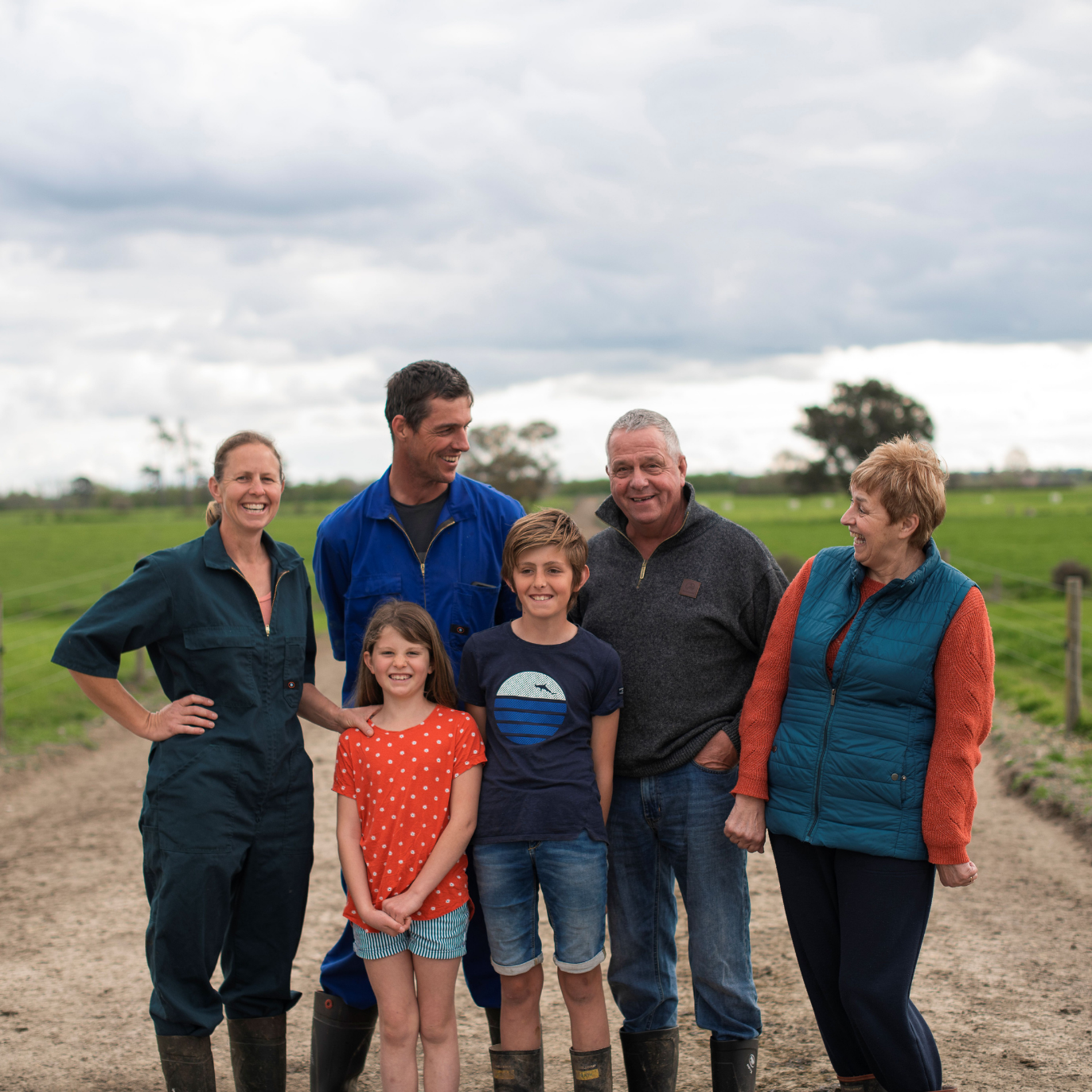 Five people standing together on a dirt road in a cloudy rural field