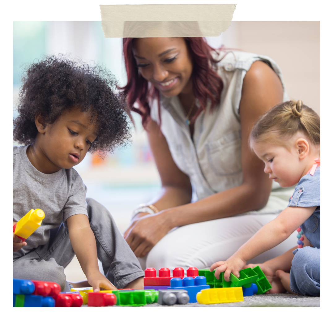 A Black woman smiles while watching two young children, one Black and one white, play with colorful building blocks on the floor.