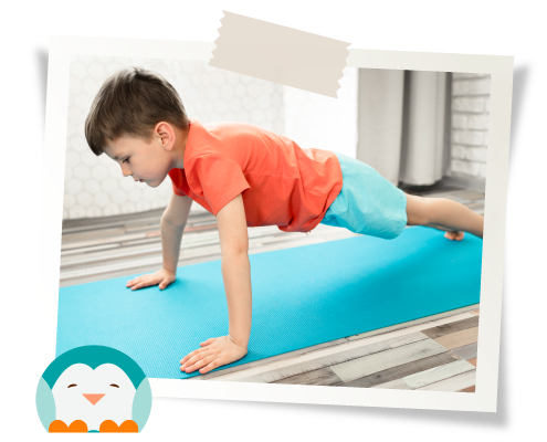 A young boy in a red shirt and blue shorts doing a push-up on a blue mat indoors.