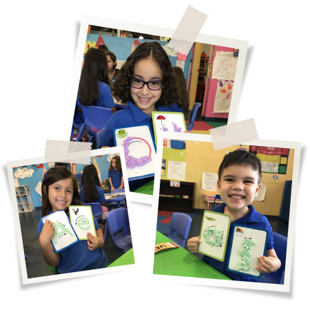 Three children in a classroom showing alphabet flashcards. They're smiling and wearing blue shirts. Two girls and a boy.
