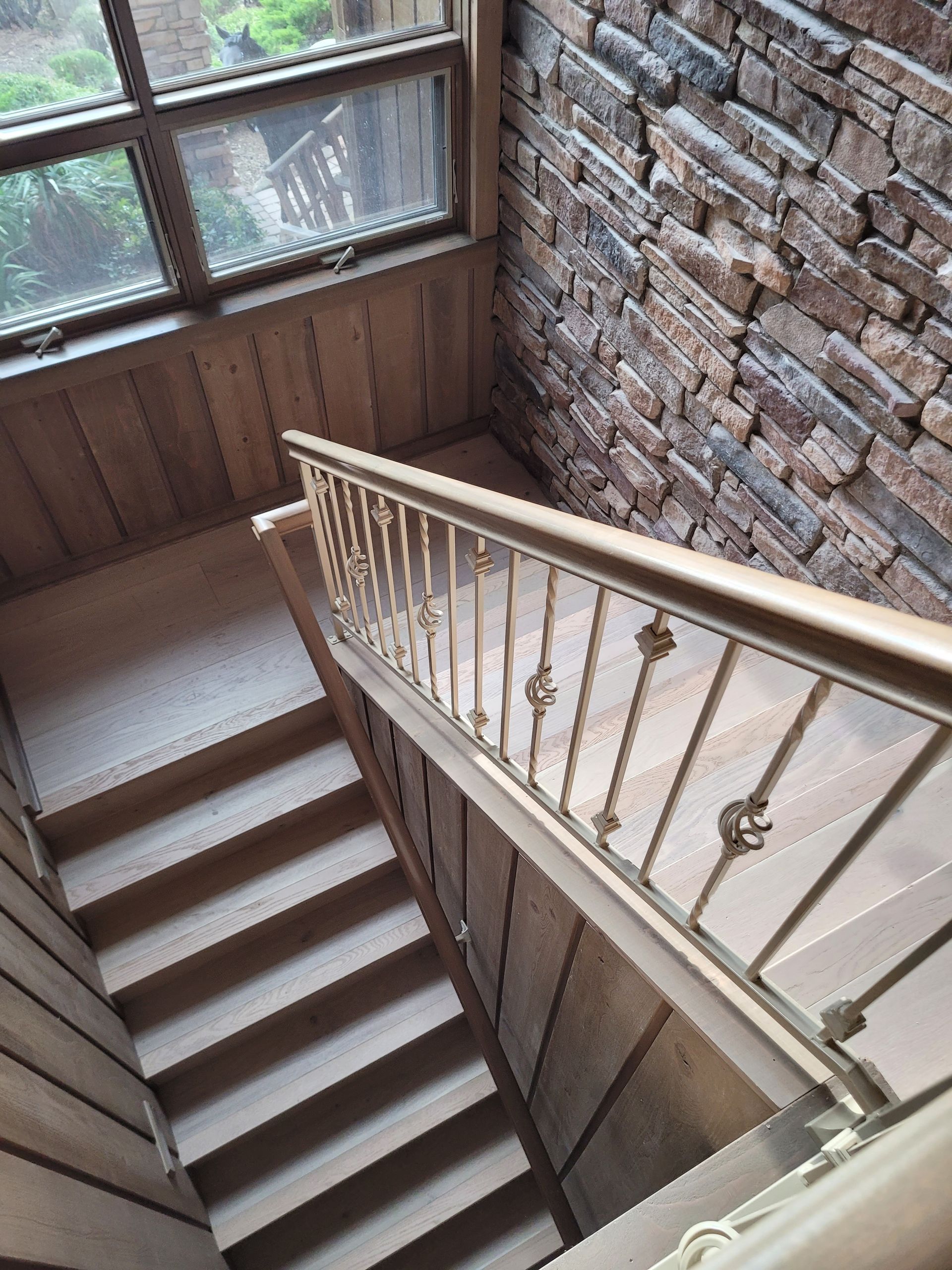 Wooden staircase descending beside a brick wall and large windows in a narrow stairwell