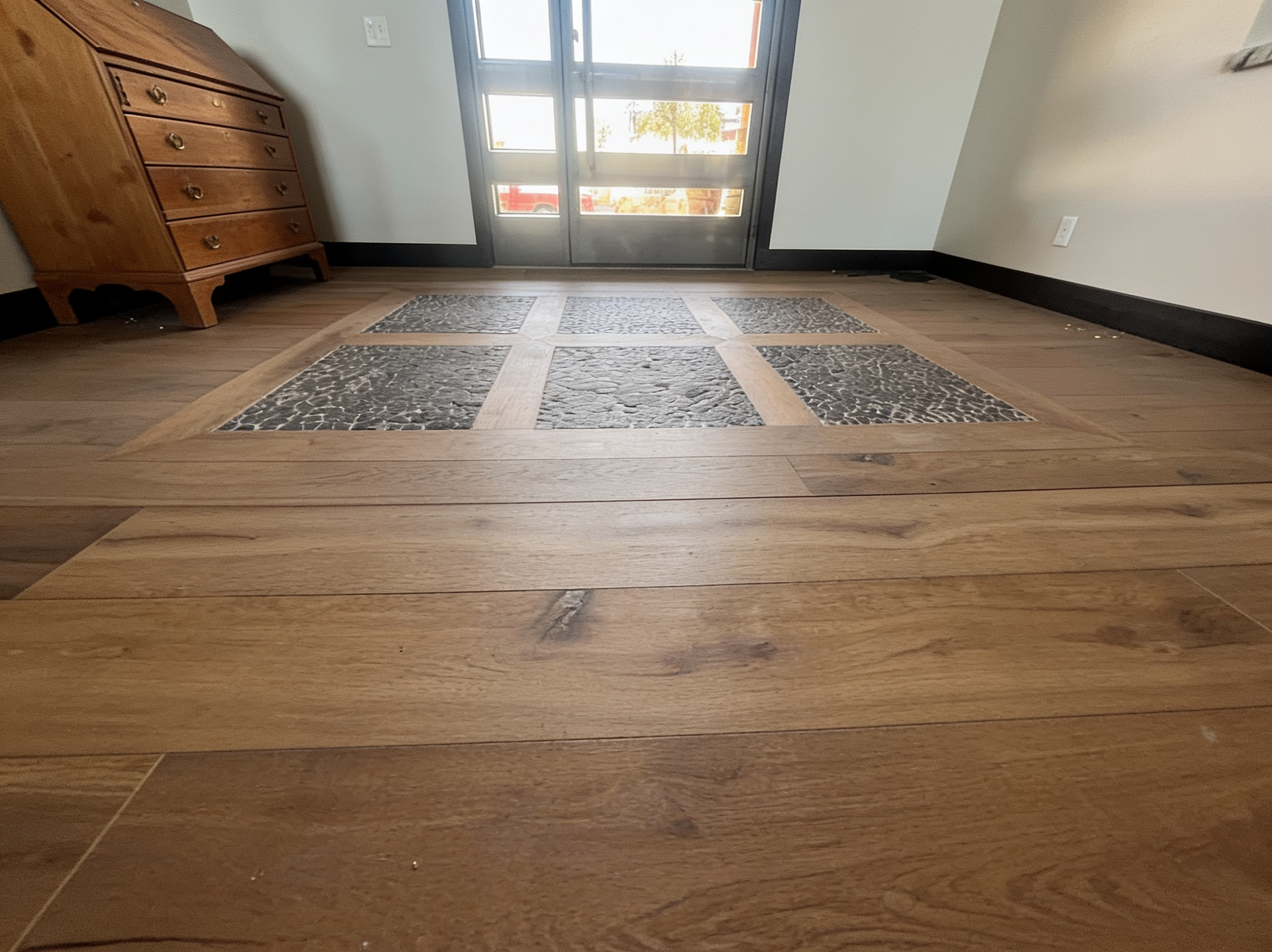 Wooden floor with three gray rugs facing a sunlit glass door, with a dresser on the left.